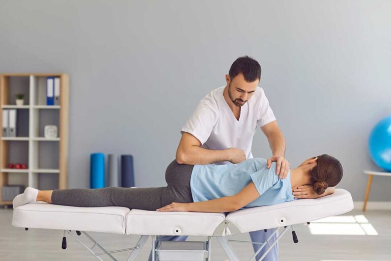 A young adult sits at a desk with slouched shoulders and a hand massaging the back of the neck.