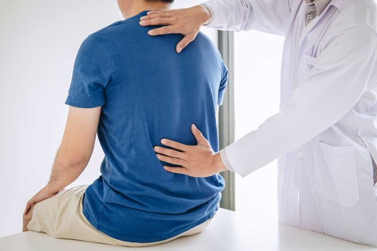 A chiropractor performing a back adjustment on a patient in a bright, modern therapy room.